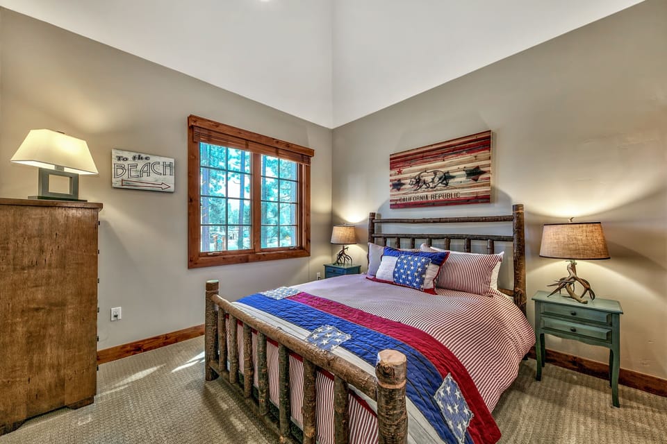 Drift off in your cozy rustic bedroom with patriotic touches and peaceful forest views through charming windows.