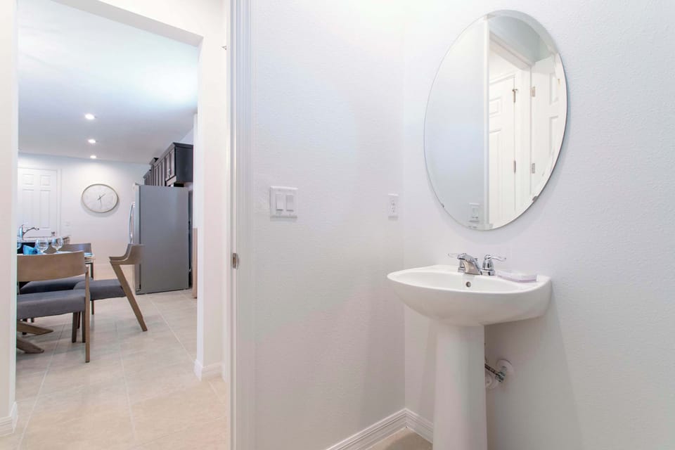 Convenient main-floor powder room with a sleek pedestal sink and round mirror-bright, modern, and steps from the kitchen and dining.