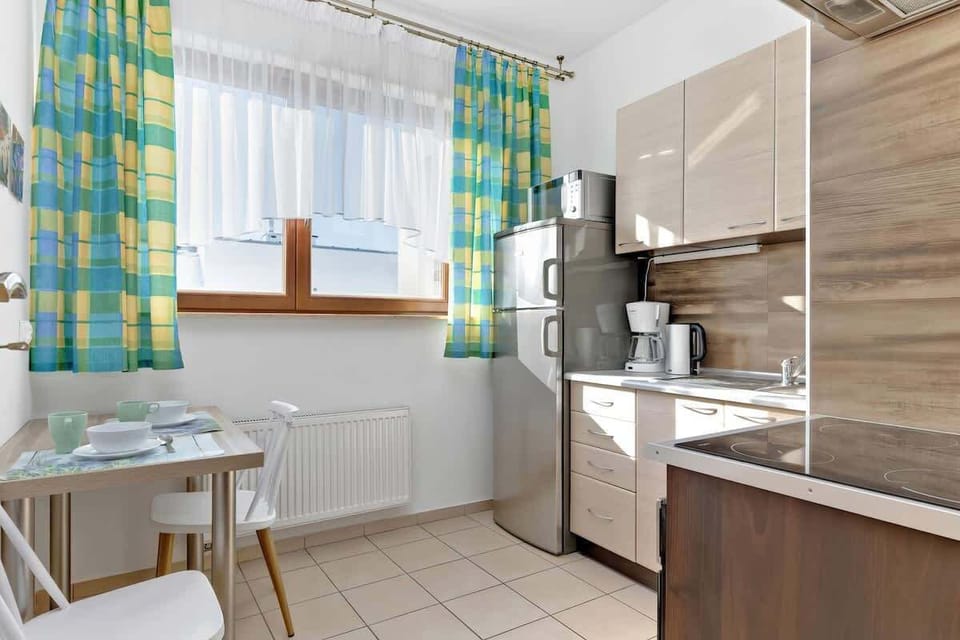 A kitchen with a large window, light-colored cabinets, and a table. The green-colored curtains add a touch of color.