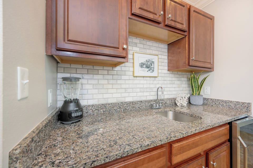 Kitchen wet bar area features granite countertops, a sleek blender, and modern cabinetry, perfect for culinary adventures