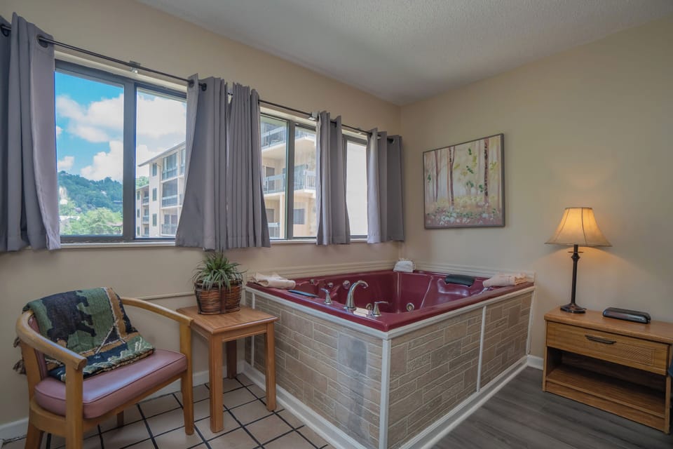 Sink into your private hot tub as sunlight streams through the windows and mountain views frame your retreat. A cozy chair and warm lighting set the scene for ultimate relaxation.