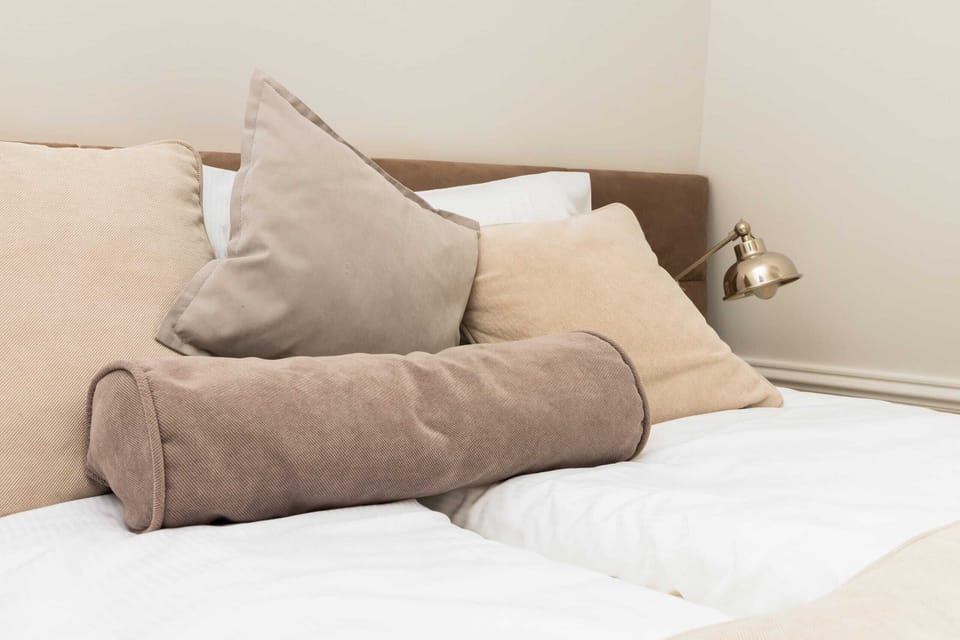 A close-up of the bedroom, focusing on the bed's decorative cushions and soft, inviting bedding.

