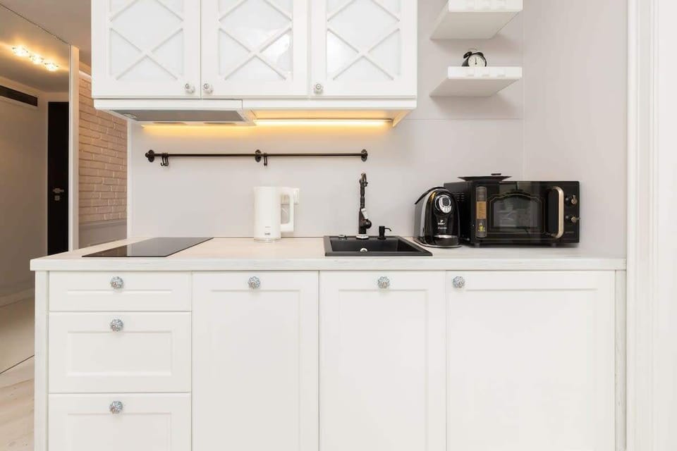 A sleek kitchen with white cabinets, wooden countertops, and appliances like a microwave and coffee machine. The space is functional and stylish.