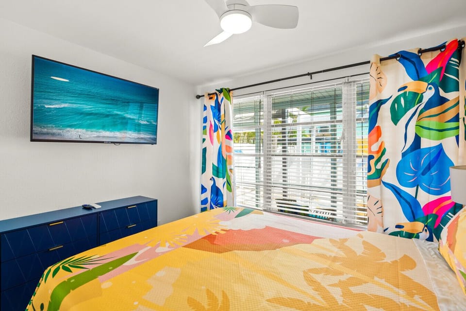 Siesta Key seaside escape featuring sunset bedding, TV with ocean views & bold curtains—designed for relaxed comfort and effortless coastal style.