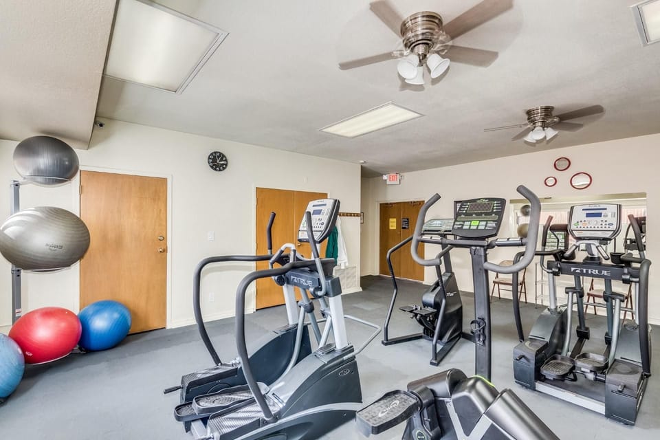 Exercise balls and cardio machines fill this fitness room with mirrored walls and ceiling fans overhead.