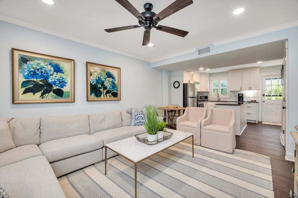 Living room with floral artwork, sofa, and kitchen view