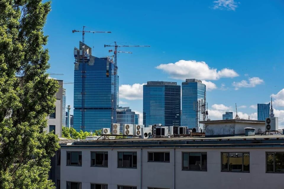 An exterior shot showing a modern city skyline with high-rise buildings. A tree-lined street adds to the urban aesthetic.