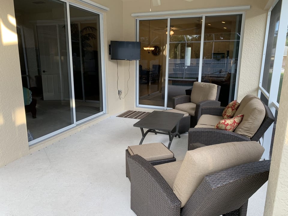 lanai with wicker reclining chairs, hassocks, sofa and TV