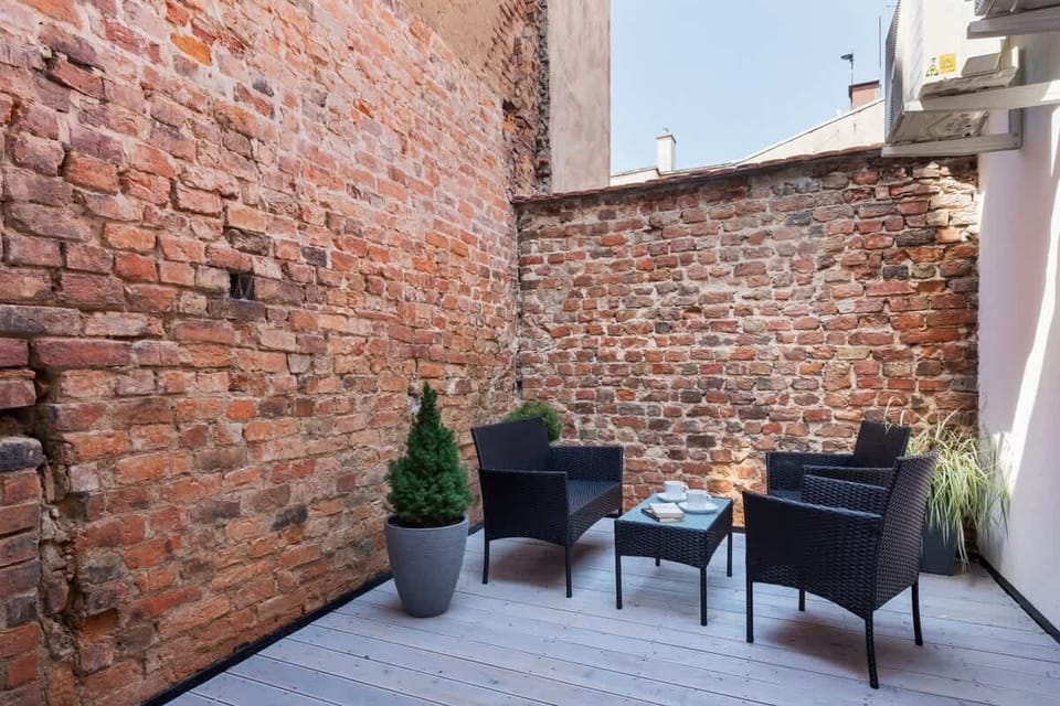 A small outdoor patio area featuring black chairs, a table, and a decorative brick wall backdrop.