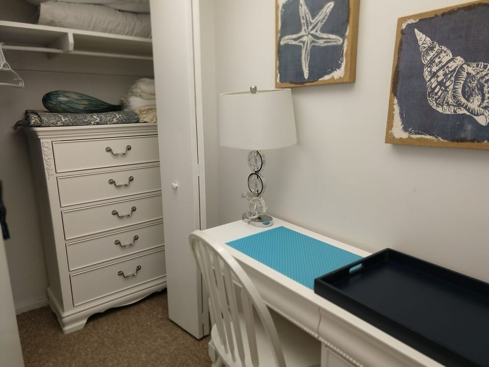 Walk-in closet has a small desk, dresser, and extra linens