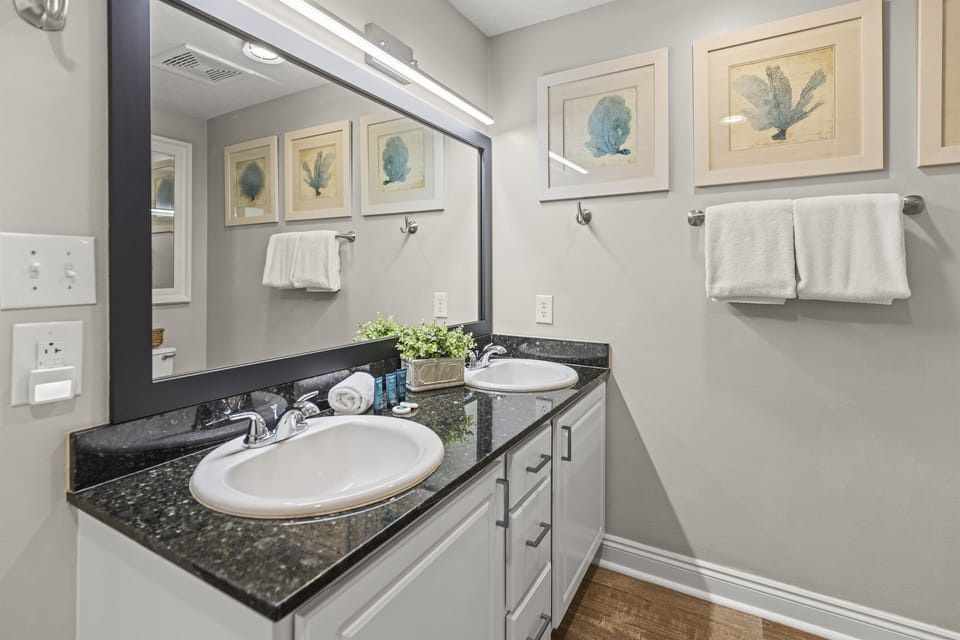 Your bathroom features dual sinks with granite countertops, soft lighting, and coastal artwork creating a spa-like retreat.