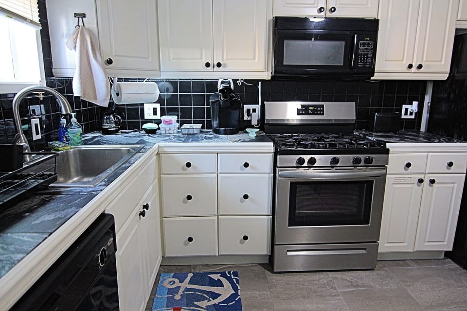This fully equipped kitchen features stainless steel appliances, black tile backsplash, and ample cabinet space. Enjoy the gas stove, microwave, dishwasher, and coffee maker. Nautical touch adds charm, making it perfect for cooking during your stay!