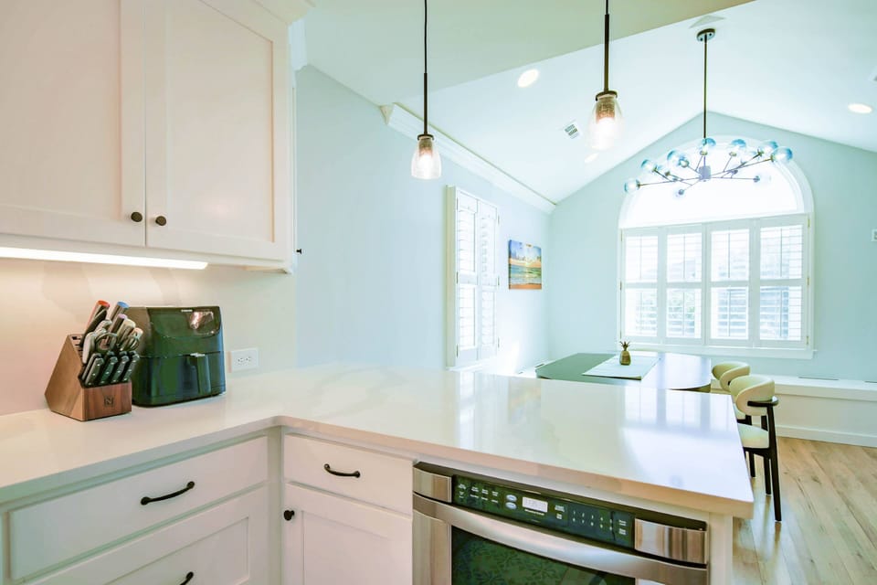 The kitchen opens into the dining room with a wall-mounted TV and lovely natural light.