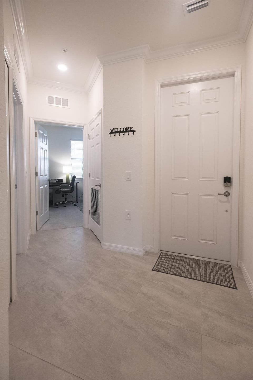 Entryway with large beige floor tiles, white paneled door, and a "WELCOME" wall hook rack.
