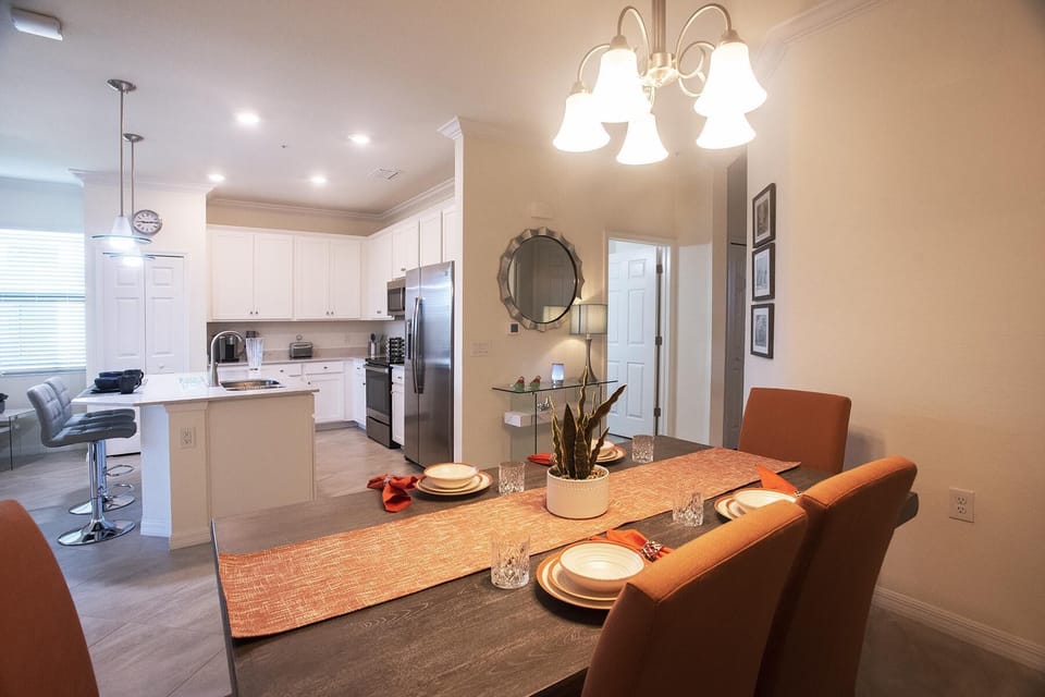 Dining area with dark wood table, orange cushioned chairs, and a chandelier over woven runner.