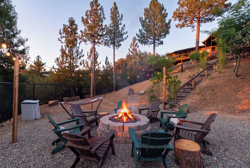 Cozy hillside fire pit with Adirondack chairs, string lights, and forest views