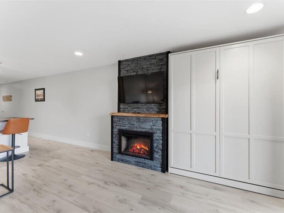Unwind in your open living space, where a stone-clad fireplace brings warmth and charm beneath a mounted TV, while sleek built-in wardrobes keep everything tidy and within reach.