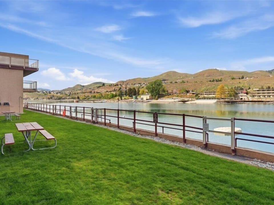 Tranquil lakefront setting with expansive lawn, mountain backdrop, and picnic area perfect for relaxation and outdoor dining.