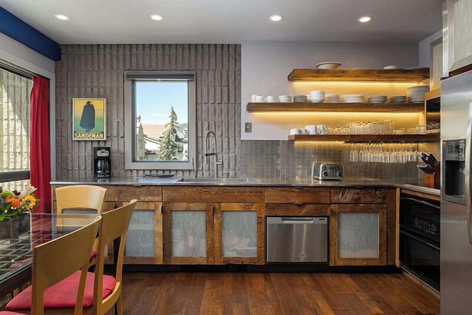 Your modern kitchen blends rustic warmth with contemporary style, featuring custom wooden cabinetry, illuminated open shelving, and stainless steel appliances—all framed by mountain views through the window.