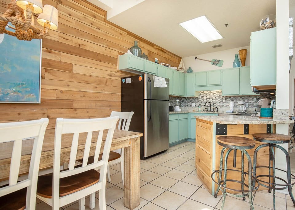 The inviting kitchen features mint green cabinetry, a rustic wooden dining table, and a cozy breakfast bar with stools