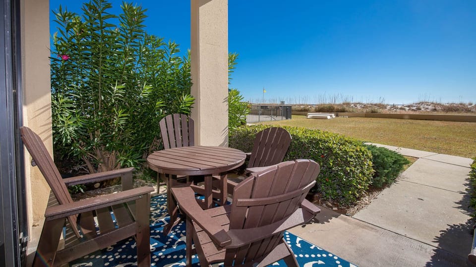 Cozy outdoor patio area features a round table and four wooden chairs, surrounded by lush greenery and a clear blue sky