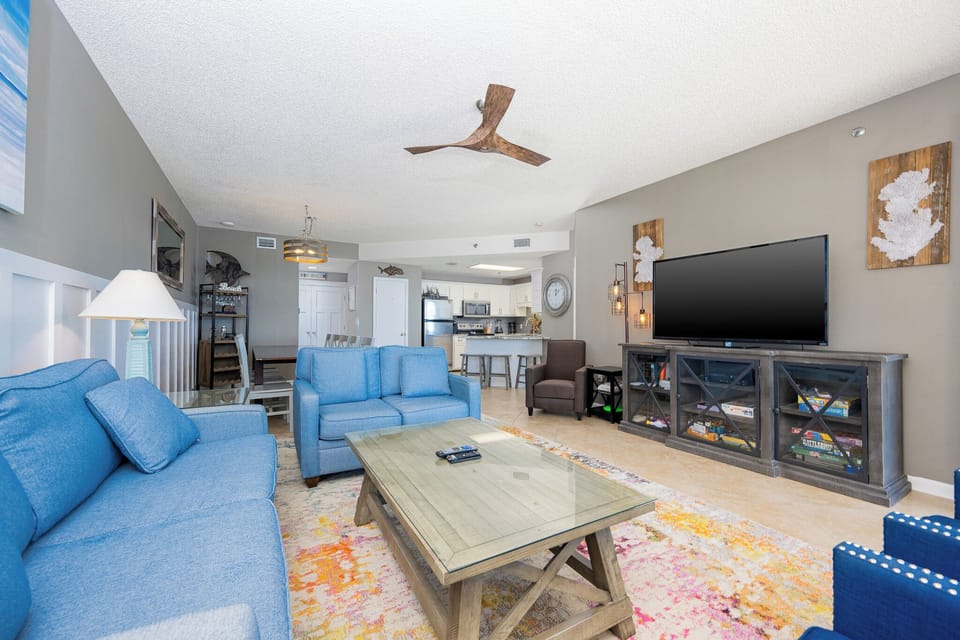 Bright living area features blue sofas with a queen sleeper and a large TV, with a view into the modern kitchen beyond