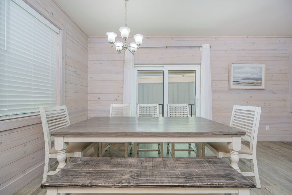 Dining area featuring a rustic table, five white chairs and a bench, and large windows for natural light