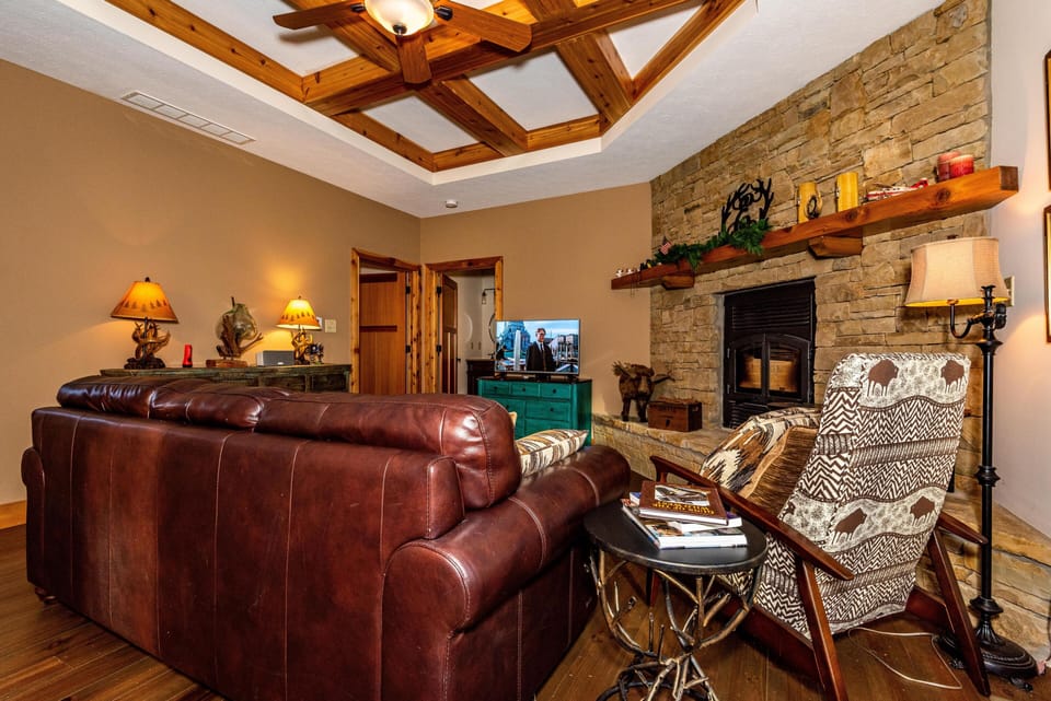 Living room with brown leather sofa, patterned armchair, stone fireplace, and wooden coffered ceiling.