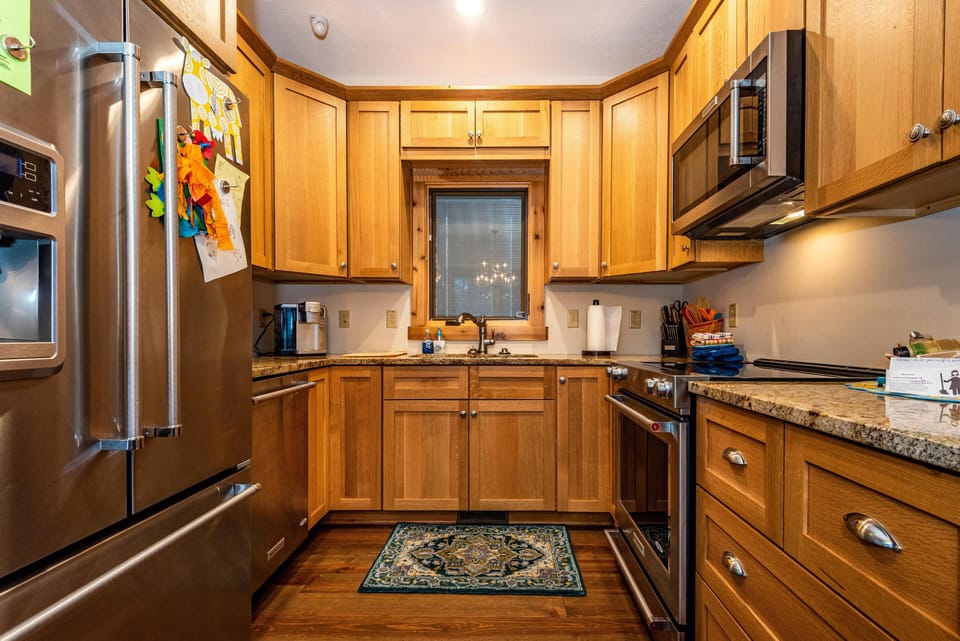 Kitchen features honey-toned wood cabinets, granite countertops, stainless steel appliances, and a patterned rug.
