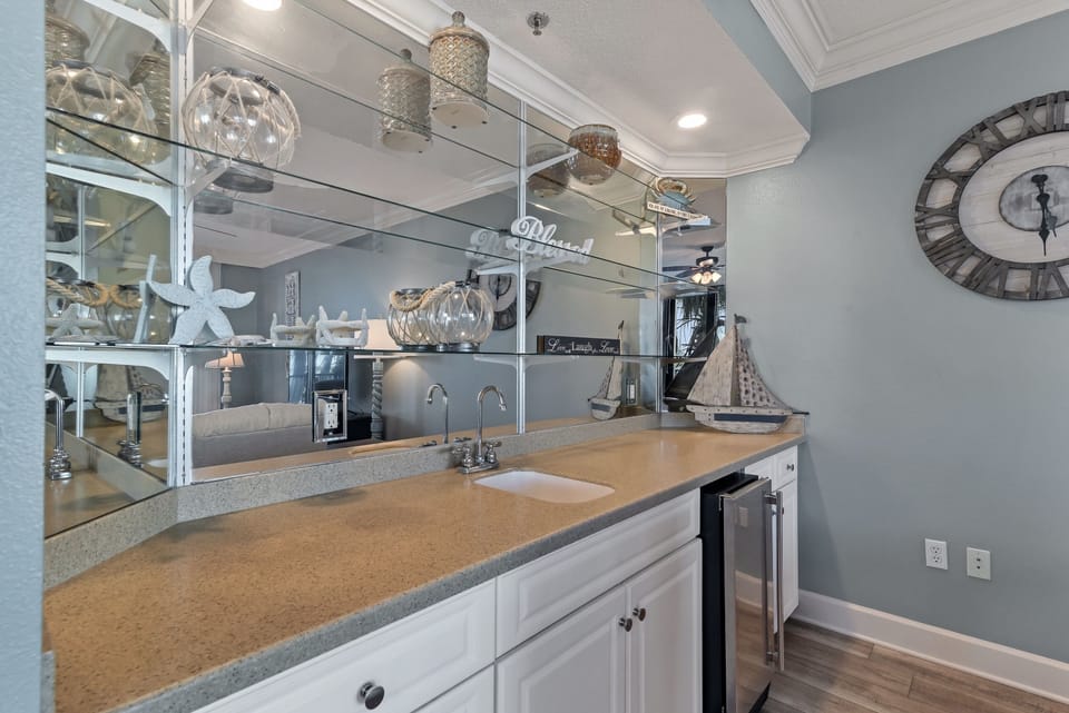 Perfect for entertaining, this stylish wet bar features a mini-fridge and a sink for convenience. With beautiful coastal decor and a reflective mirror backdrop, it's a dedicated space to mix drinks and toast to a perfect getaway.