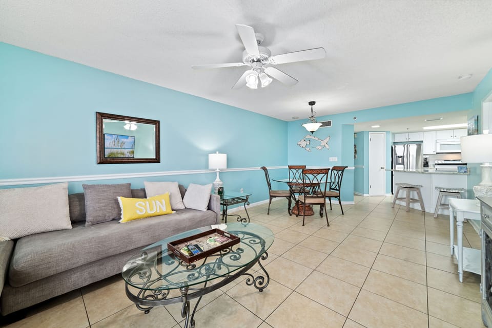 Functional and lively. This open-concept space seamlessly combines the living room, dining area, and breakfast bar, all set against a stunning aqua backdrop and easy-to-clean tile flooring.