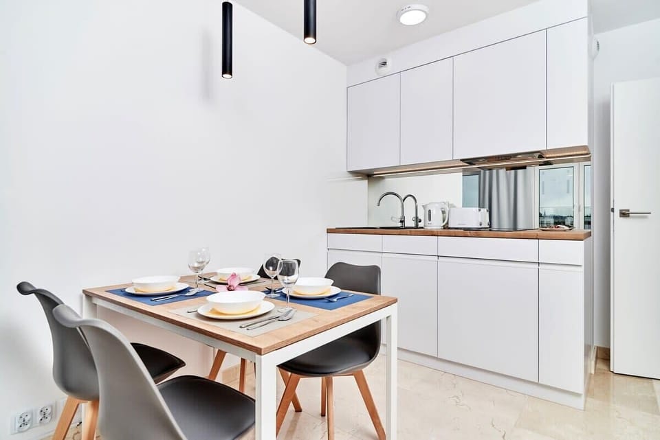 A clean and minimal kitchen with a table for four, elegant decor, and bright overhead lighting.