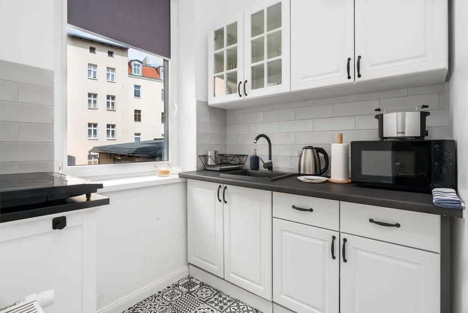 A compact kitchenette with white cabinets, a dark countertop, and modern appliances like a kettle and microwave.