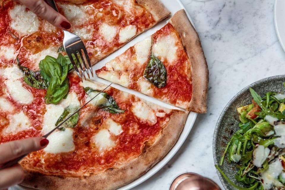 Margherita pizza with fresh basil and a side salad served on a marble table