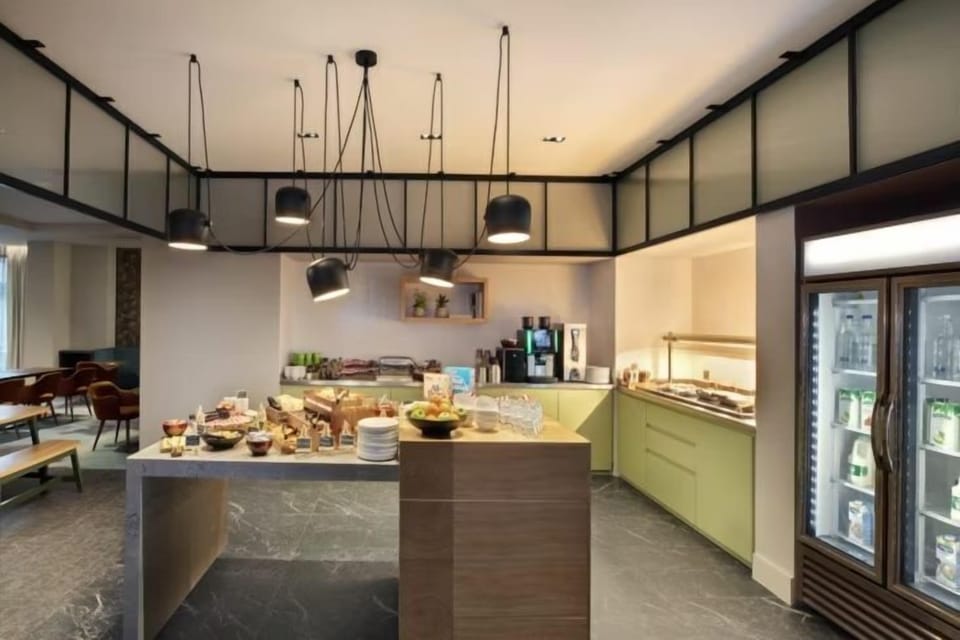 Breakfast island counter with fruit, pastries, a coffee machine, juice dispenser, and refrigerated drinks display