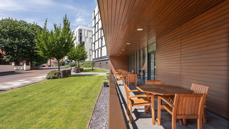 Outdoor patio seating with wooden tables framed by lawn and trees.