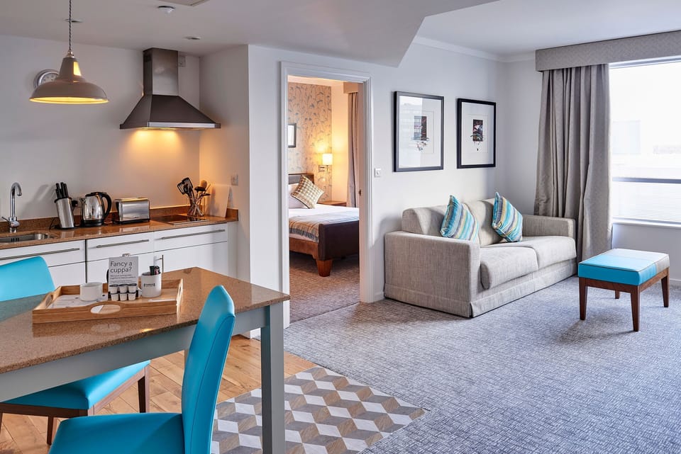 Bright living area with a sofa, kitchen, and door to the bedroom.