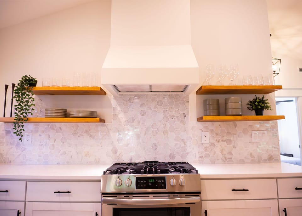 Gas stove and open shelves with plenty of dishware, glassware, and coffee mugs