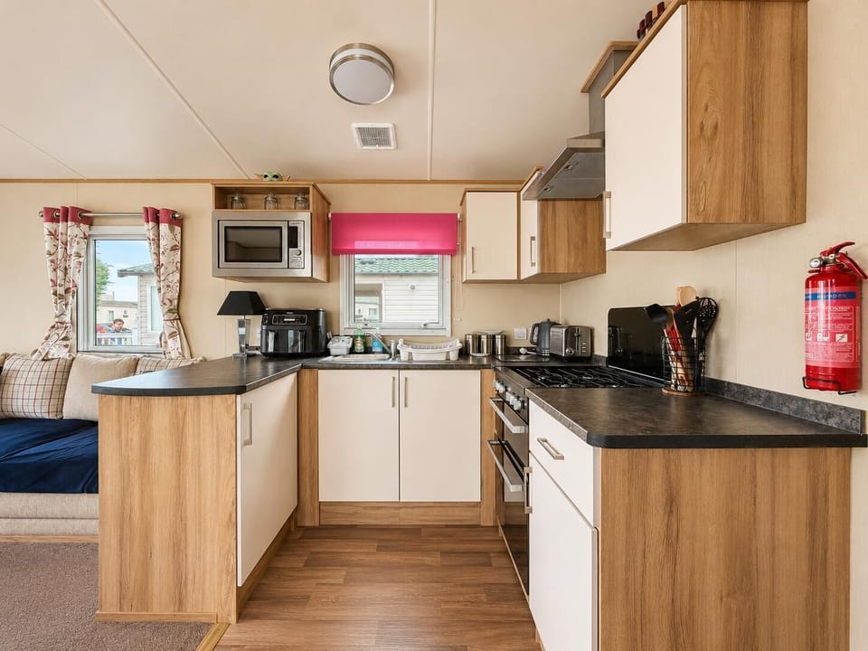 U-shaped kitchen with wood-effect cabinets, black countertops, and a window dressed with a bright pink blind.