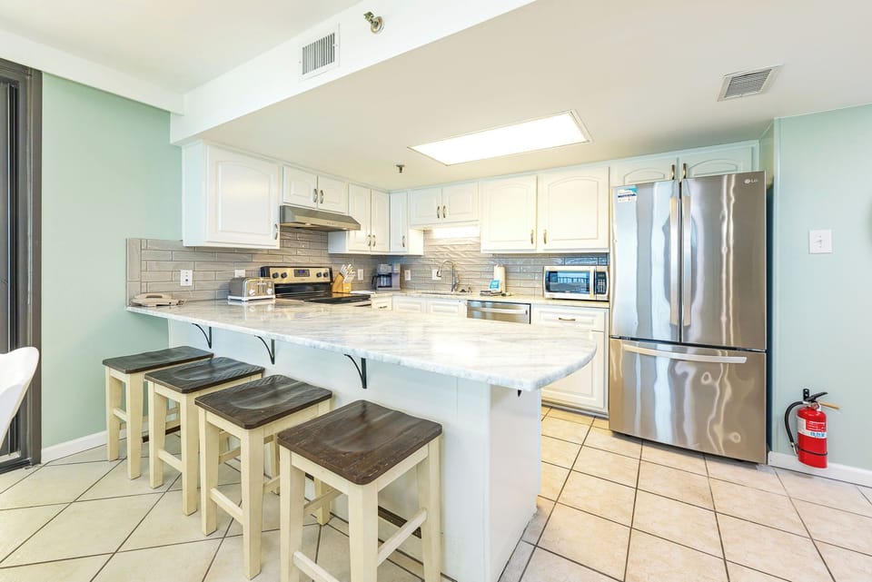 Bright kitchen featuring white cabinetry, a marbled countertop, and a breakfast bar with wooden stools for casual dining