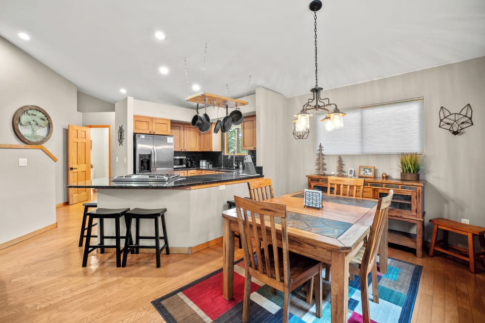 Open-concept dining and kitchen area featuring a rustic wooden dining table, modern light fixture, and a granite breakfast bar with barstool seating—perfect for family meals and entertaining.