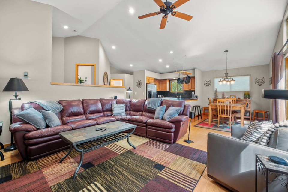 Bright and inviting living space featuring a large leather sectional, vaulted ceiling with ceiling fan, and seamless flow into the kitchen and dining areas. Perfect for entertaining or relaxing after mountain adventures.