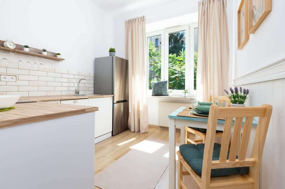 A dining area with a wooden table and chairs, positioned near a window that brings in natural light. The setup is simple and inviting.