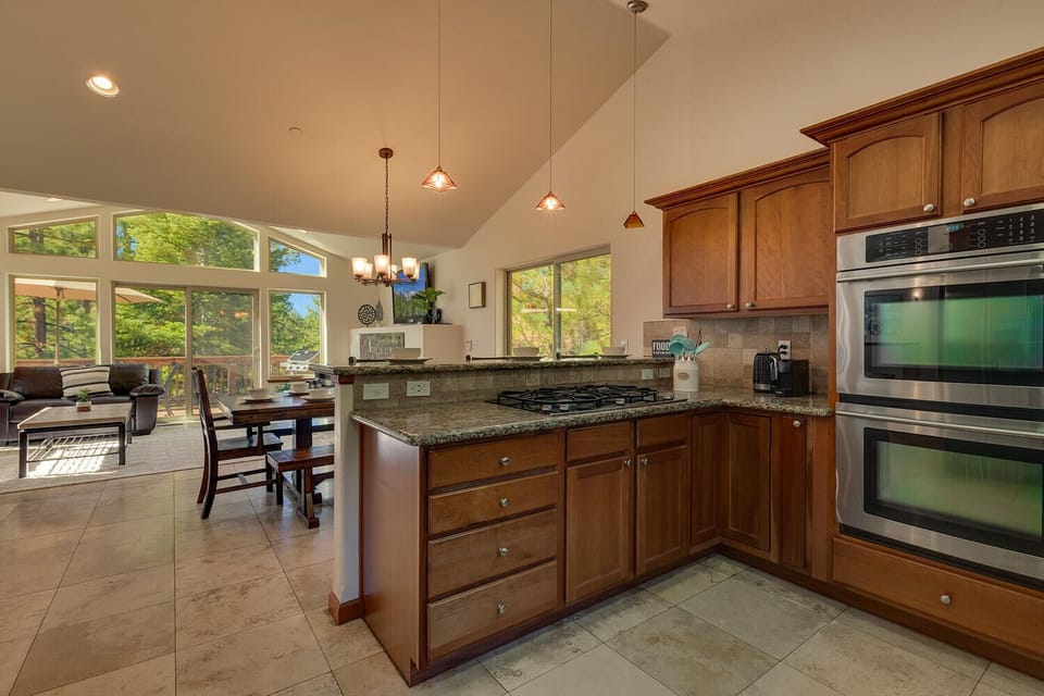 - Open concept kitchen with breakfast bar and seating  
- Granite counters with modern double ovens and stove  
- Connected to dining and living room with forest view
