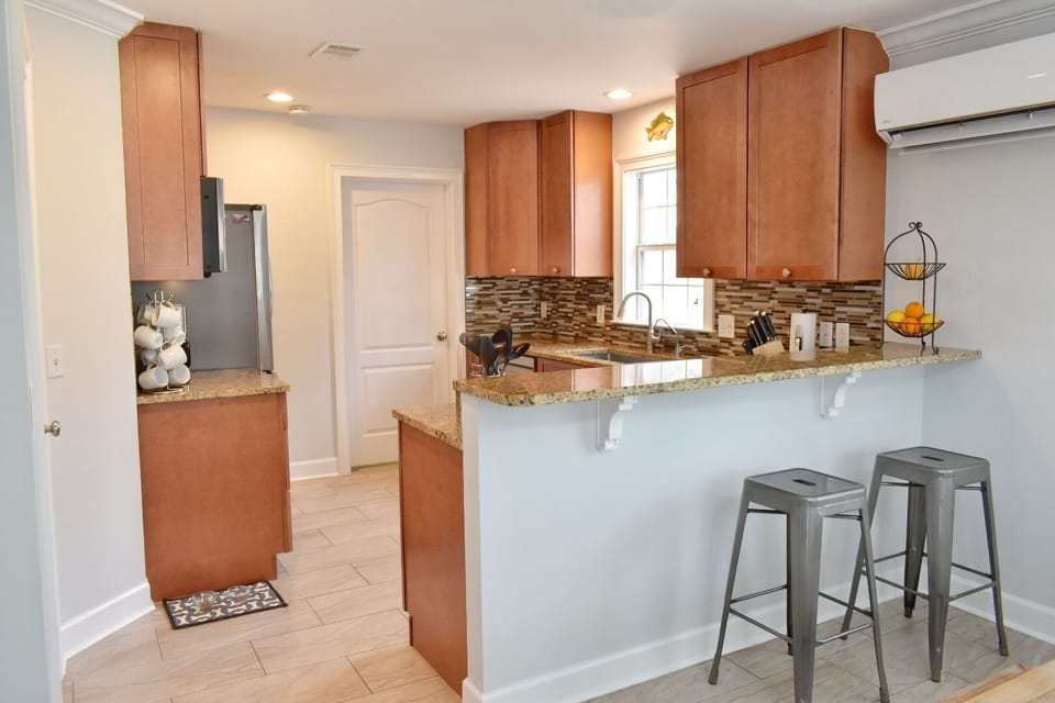Stocked chef's kitchen next to dining with utensils, serving dishes, & bakeware.