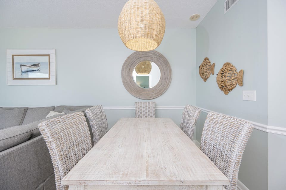 Dine comfortably at the rustic table surrounded by woven chairs and charming coastal decor for a relaxed atmosphere