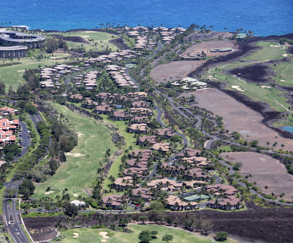 Aerial view of a sprawling oceanside resort community with golf course fairways, residential clusters, and coastal access along the shoreline.