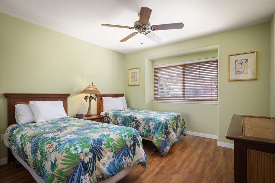 Your tropical-themed retreat awaits with two plush beds draped in vibrant island florals, soft lighting, and a ceiling fan to keep you cool and comfortable throughout your stay.