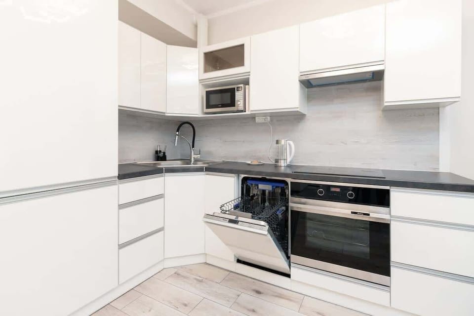 A different view of the kitchen, showing white cabinetry, a stove, and a gray backsplash. The room has a modern, minimalist design, maximizing both functionality and style.