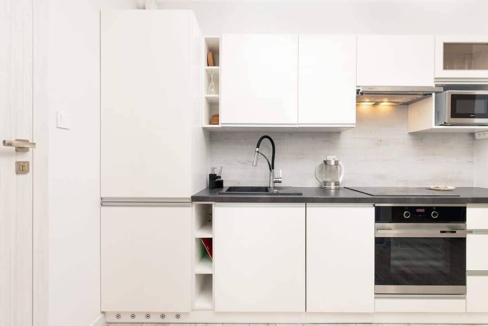 Aneks kuchA compact, modern kitchenette with white cabinets, a built-in stove, oven, and a microwave. The countertop is dark, contrasting with the clean white cabinetry. enny